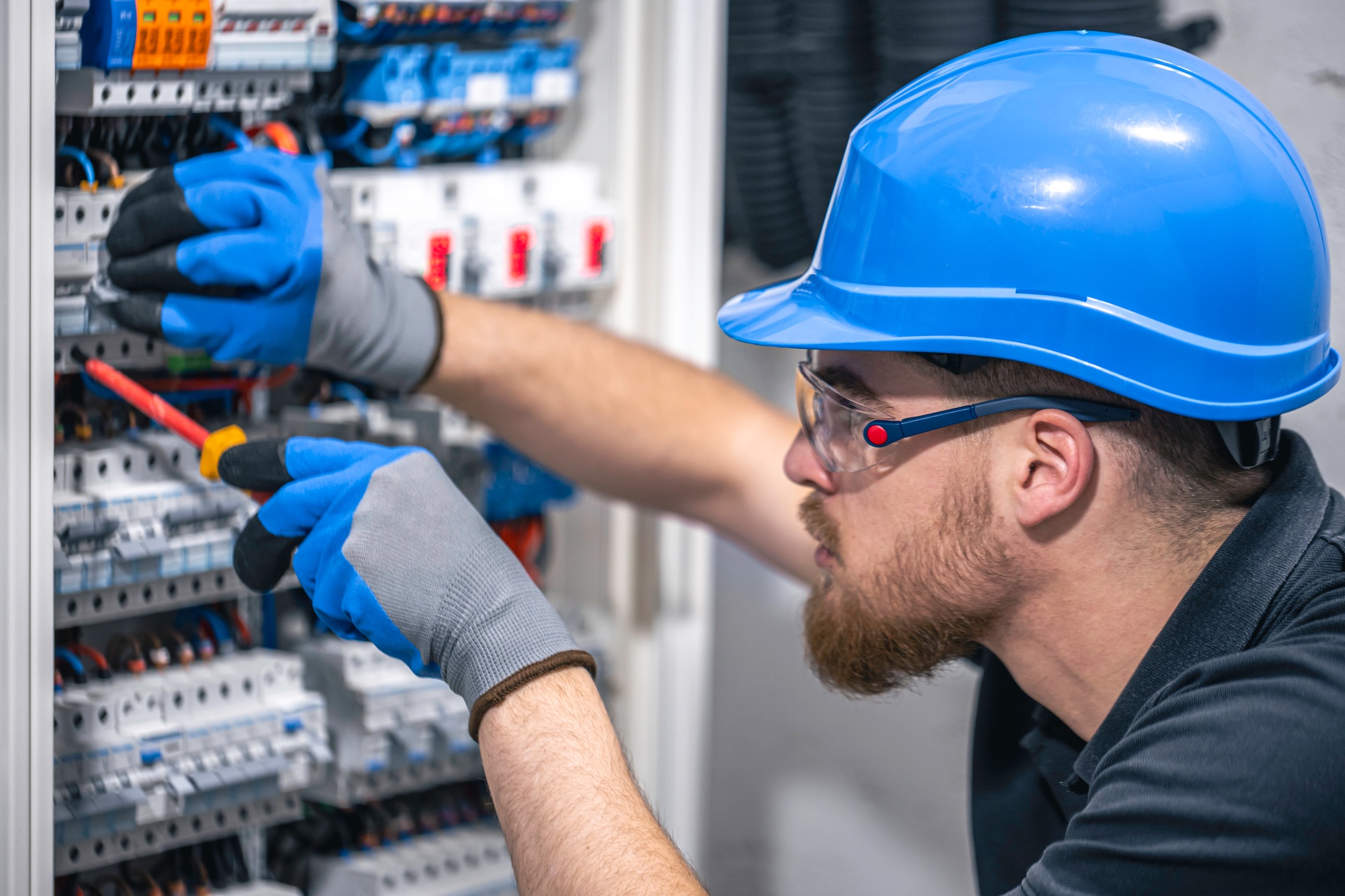A male electrician works in a switchboard with an electrical connecting cable.